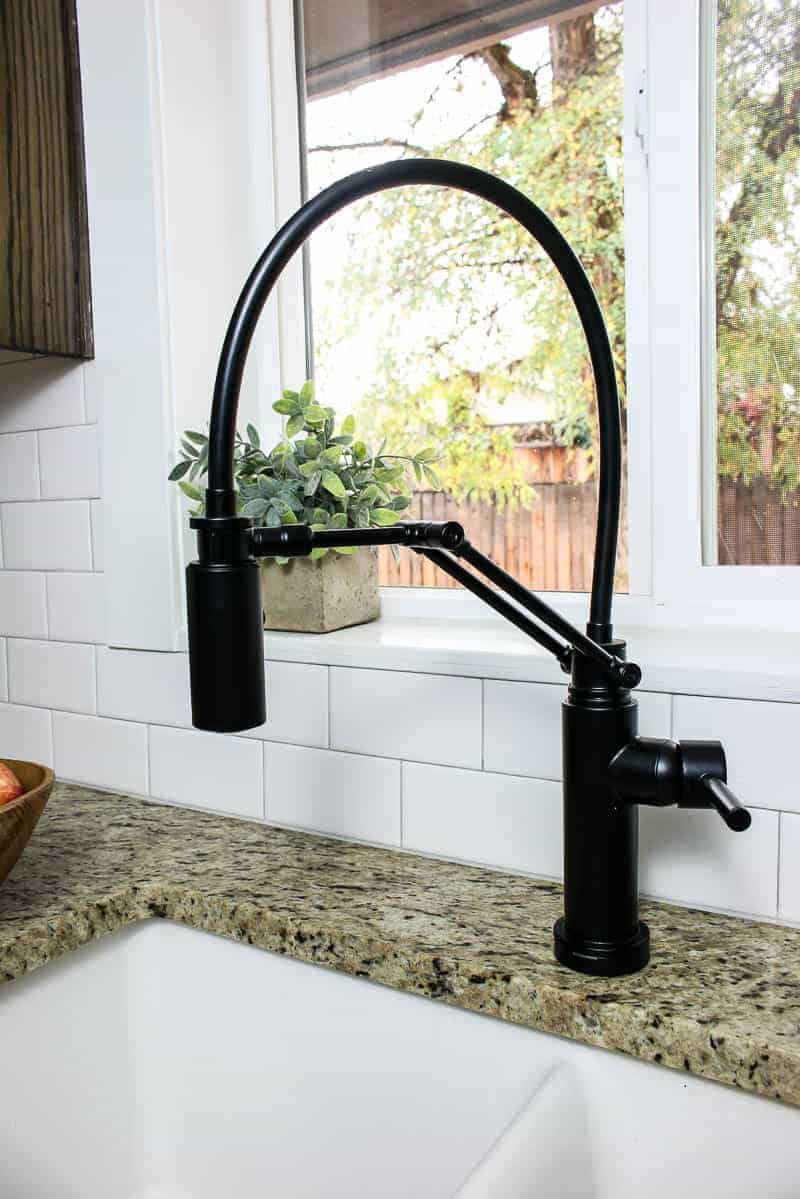 A sleek black kitchen faucet installed in an undermount sink with granite countertops