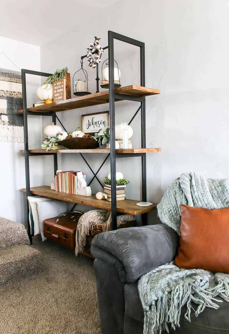 This living room bookshelf is packed with Living Room Shelf Decor that's perfect for Fall - real and faux pumpkins, gourds, books, and greenery. This shelf decor adds a touch of fall to the room.