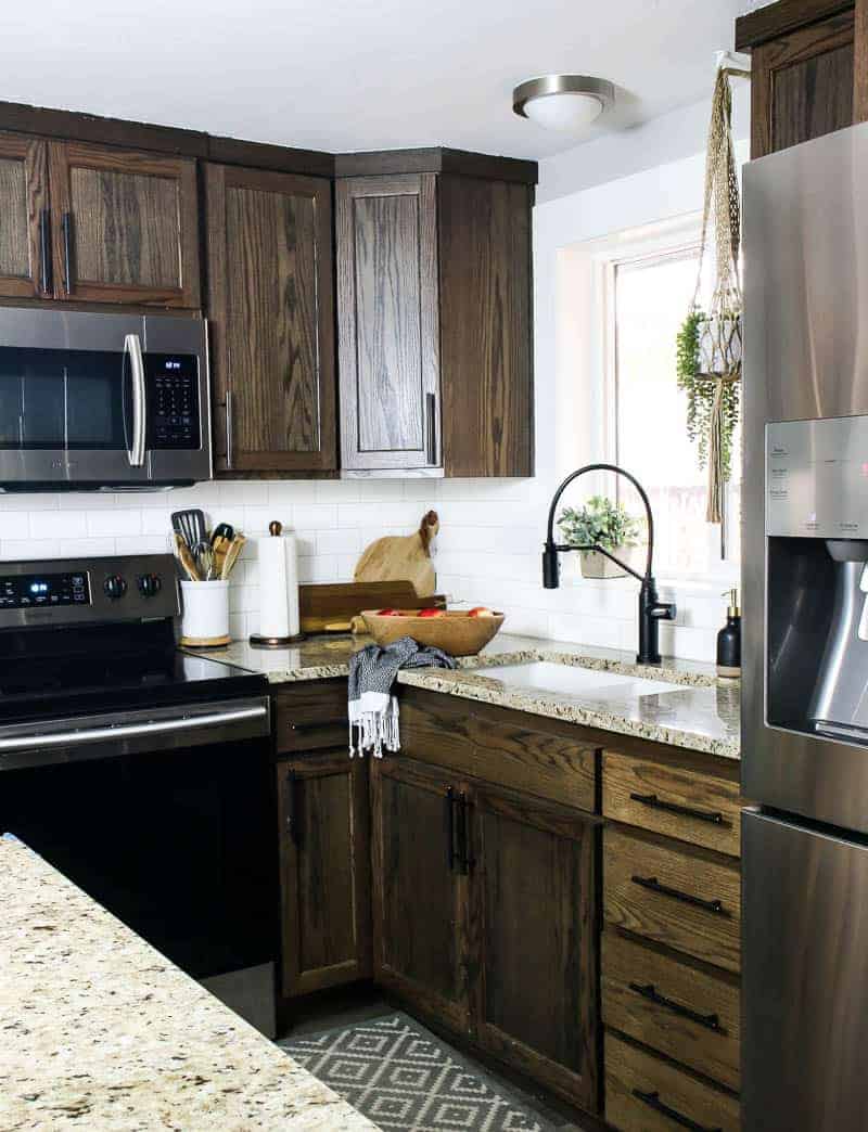 A farmhouse style kitchen with dark cabinets, granite counter tops, and a quartz undermounted farmhouse style sink