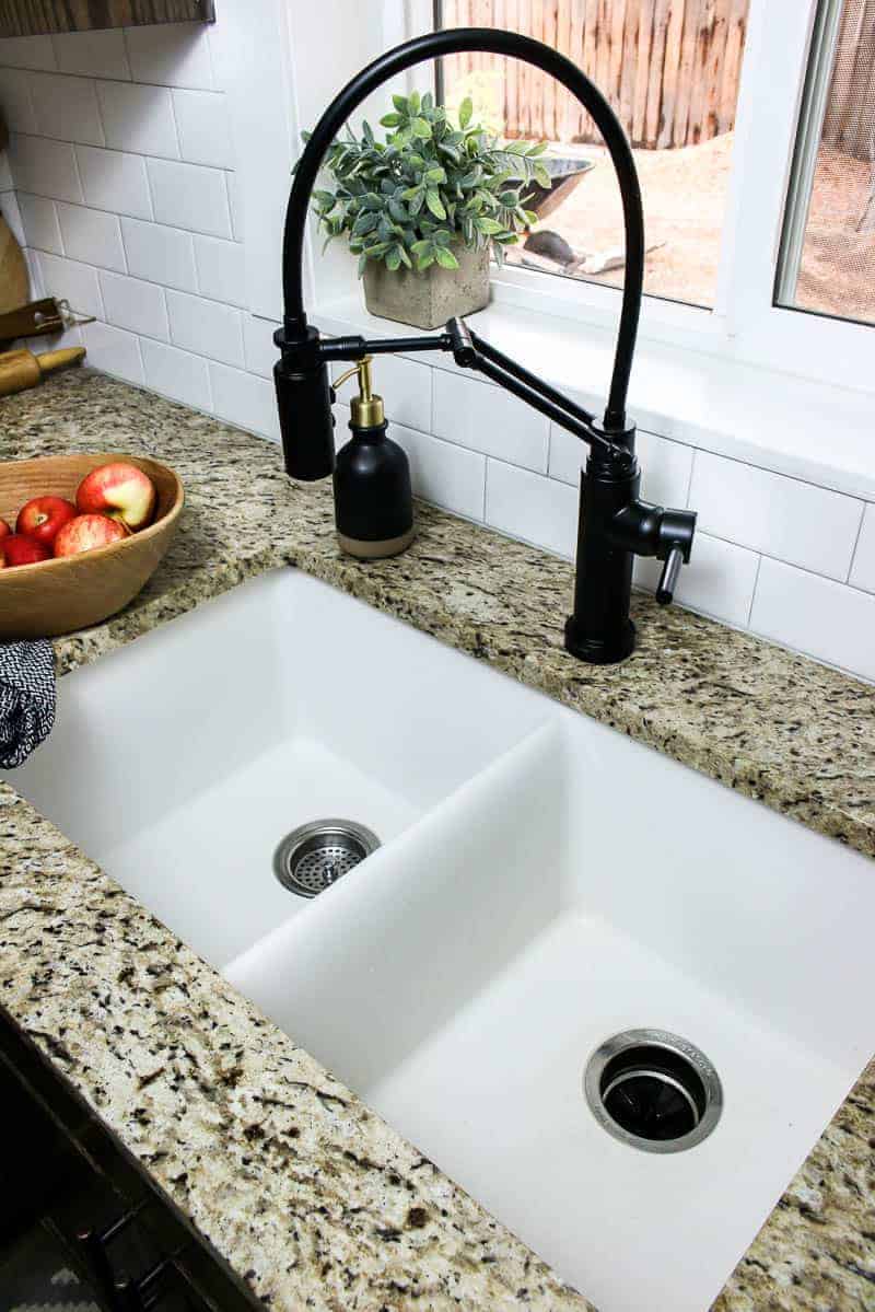 An overhead view of a white farmhouse style undermount sink with a black faucet and granite countertops