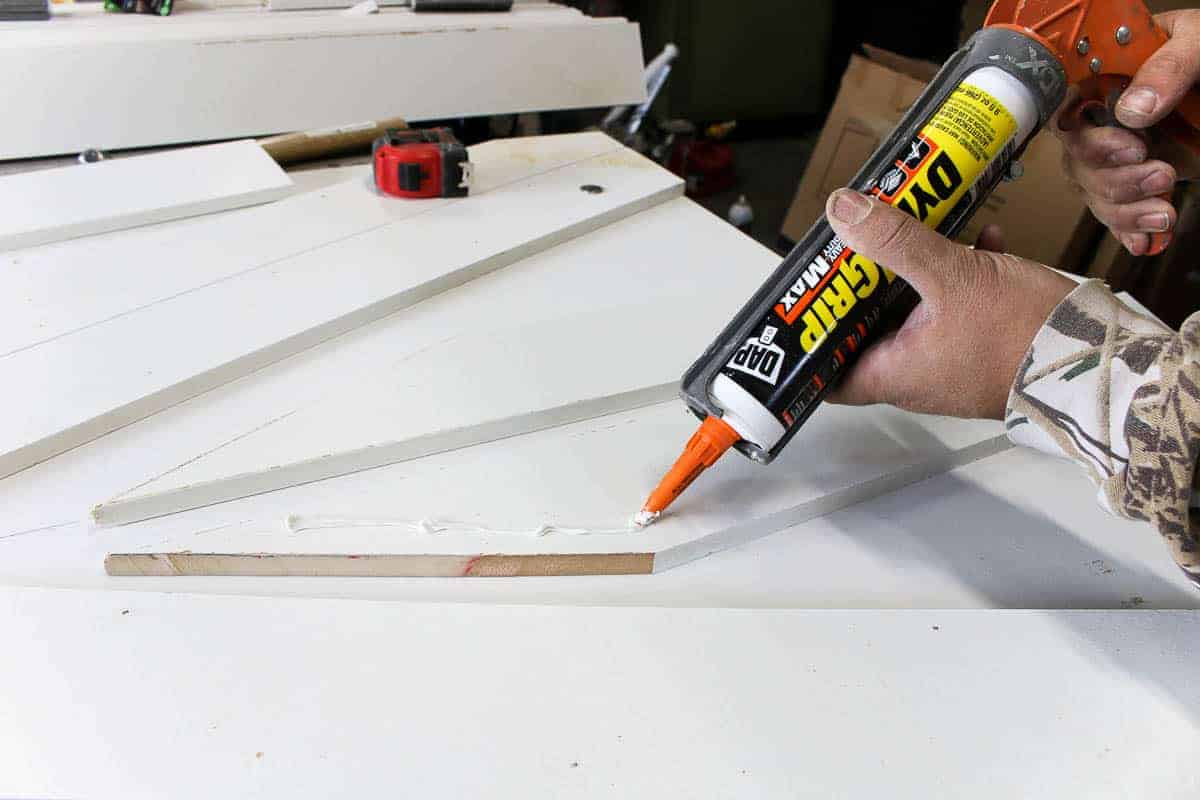 A pair of hands applies adhesive glue to diagonal cut wooden slats, which will create the signature X pattern on a wooden barn door.