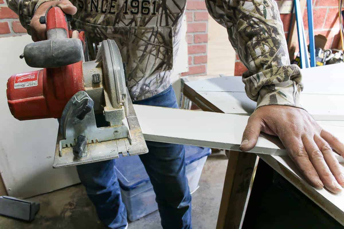 A man is using a circular saw to cut a wooden slat on a diagonal cut.