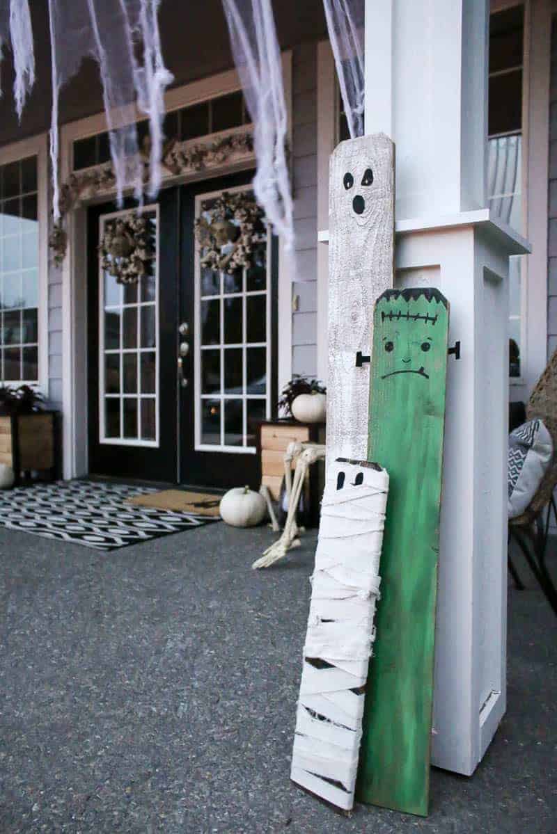 Upcycled halloween porch decorations made with fence boards painted into ghost, frankenstein and mummy to decorate a fun decorated porch for Halloween