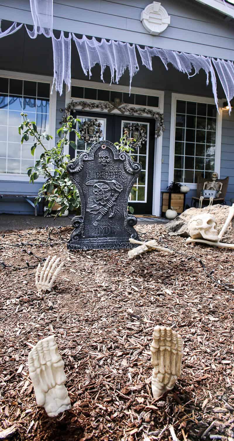 Fake gravestone on the front lawn, skeleton hands and feet with curtains in the porch roof as the Halloween Porch Decor