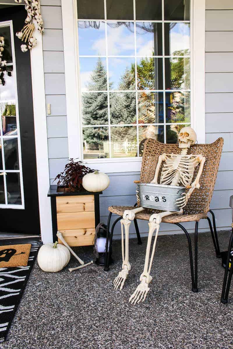 Halloween Porch Decor including pumpkins and full skeleton sitting on the porch chair.