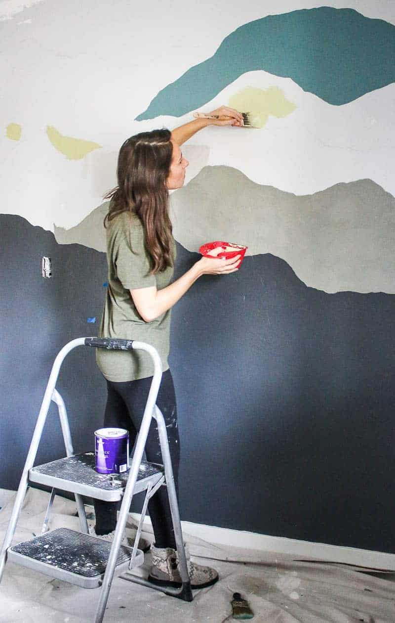 Full body shot of woman painting the fourth color of the mountain mural