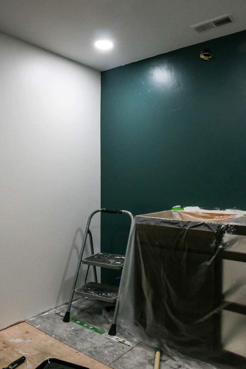 One painted teal green wall and one white painted wall with a step ladder and painting supplies.