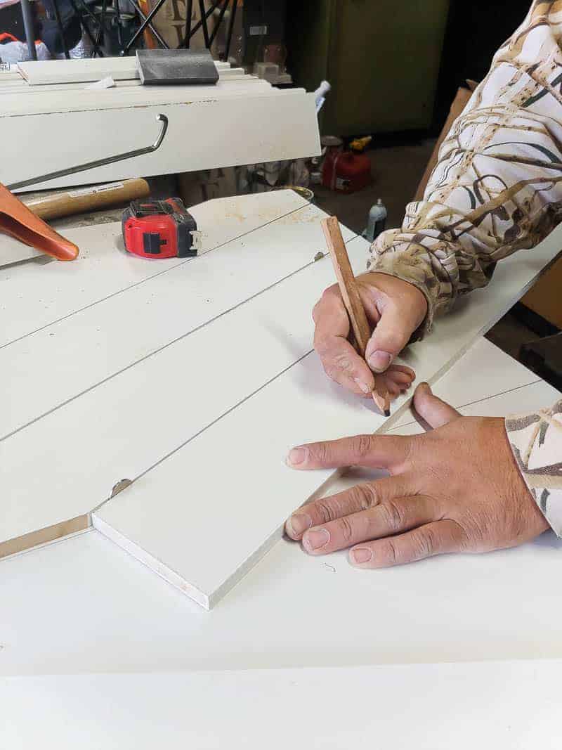 A pair of hands makes diagonal marks on the wooden barn door slats with pencil to mark where to cut to create an x design.