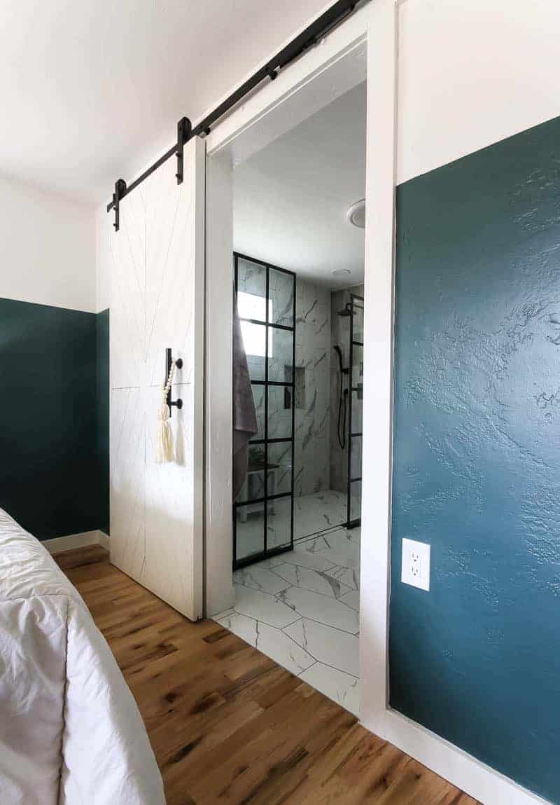 Our sliding bathroom barn door with modern black industrial hardware hangs on a white and teal painted wall.