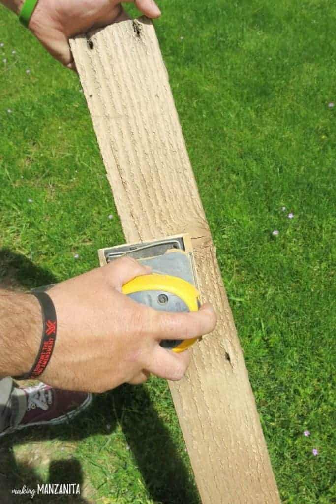 Man using a hand sander on a piece of reclaimed pallet wood to make wooden bottle opener