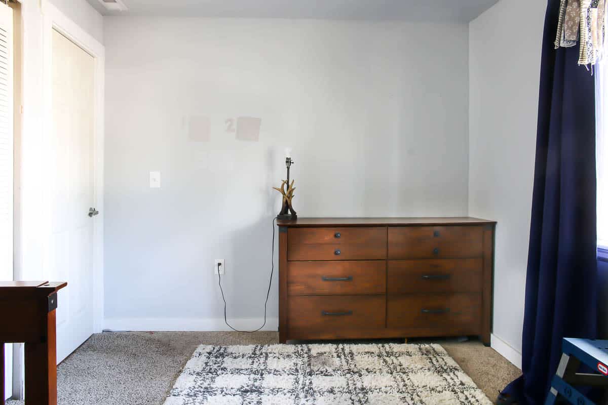 plain bedroom wall before makeover with a wooden dresser and a rug