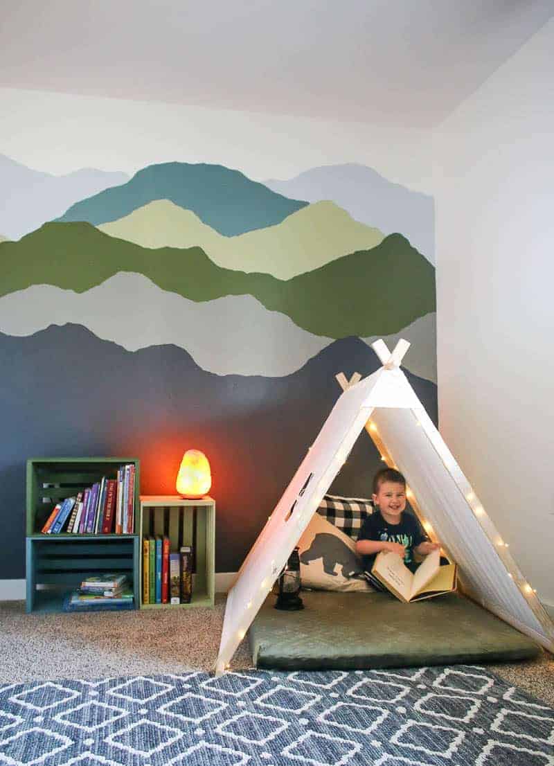 Boy sitting in the cozy nook beside the colorful pallet bookshelves and mountain mural paint