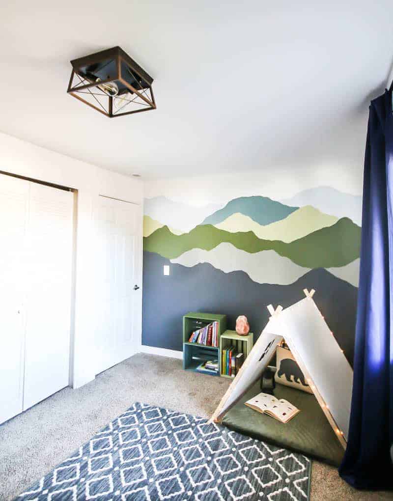 Wooden light fixture, mountain mural wall, colorful bookshelves and cozy nook.