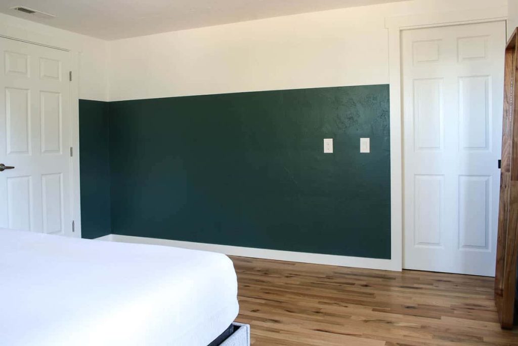 A corner of the master bedroom after renovating the closet area. The walls are painted a hunter green color with white space at the top, and there are two white doors in either corner of the room.