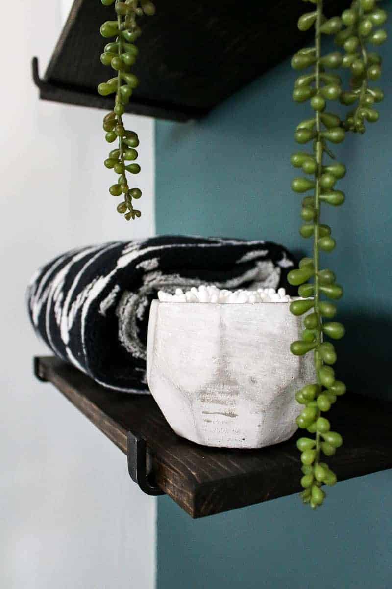 Floating wood shelves with towels folded on shelf, concrete bowl with Q-tips, and some plant accent