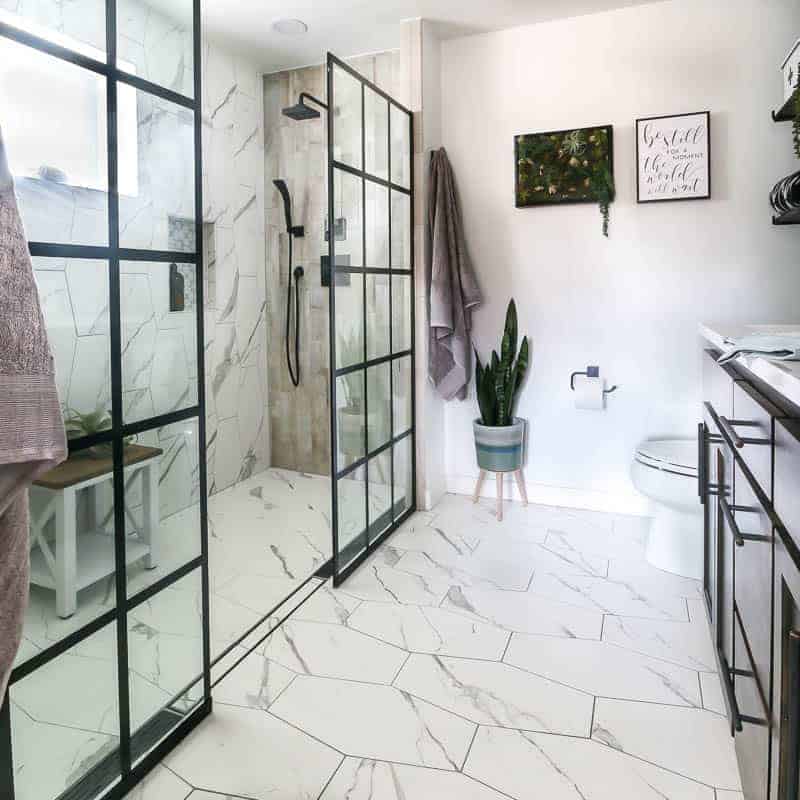 Modern farmhouse bathroom reveal showing his and her dual head shower with windowpane shower door panels, linear drains, marble tile, bathroom plants, black finishes and white wall paint