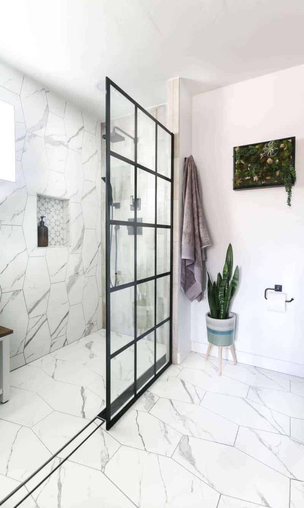 Modern looking shower with white tile and black shower head and black paneled windowpane shower doors. 