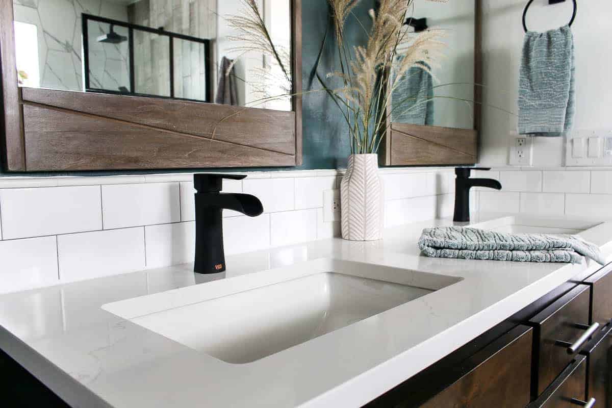 White quartz countertop on bathroom vanity with two sinks with black faucets and wooden mirrors