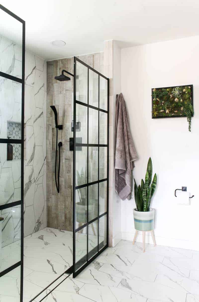 New look of the shower area with black shower system, indoor plant, hanging towels and a wall frame decor with fake succulents