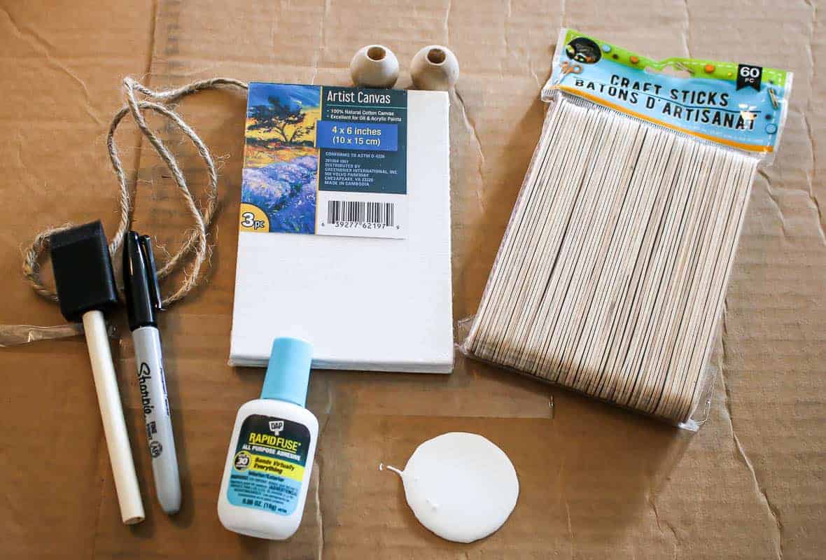 Photos of the materials including canvas, foam paint brush, sharpie, glue, white paint, two wooden beads and popsicle sticks