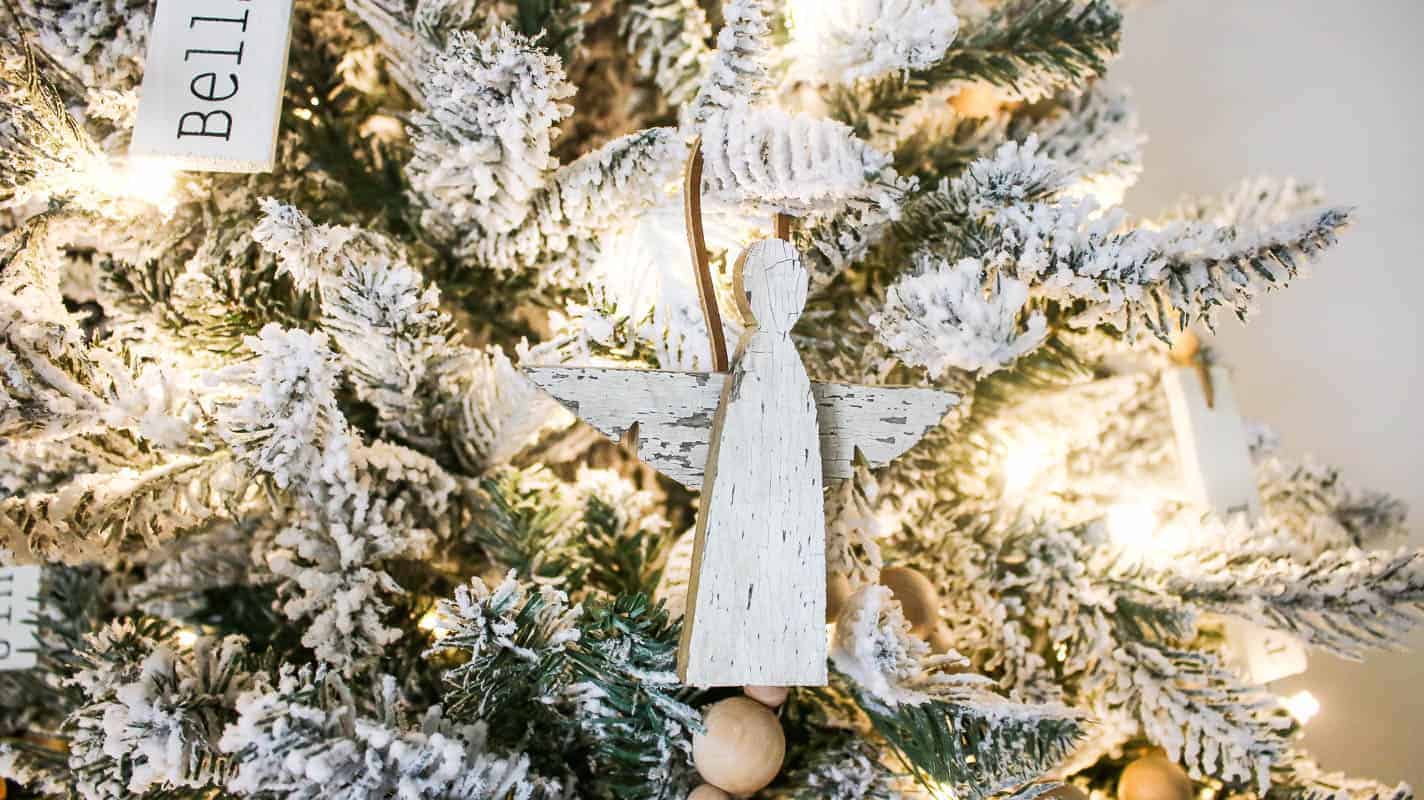 Closer look at the little barn wooden angel ornament hanging on the tree with other wooden ornaments with different names and words