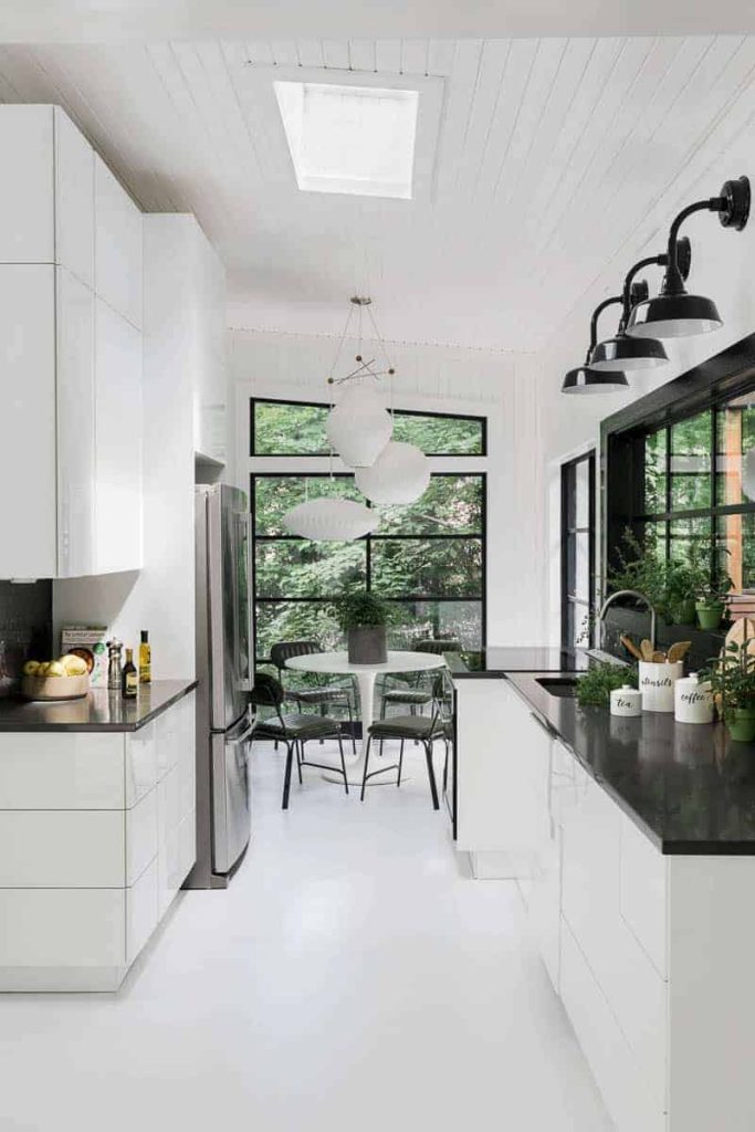Modern White kitchen with white cabinets, floors and walls with black accents and counter tops and a skylight.