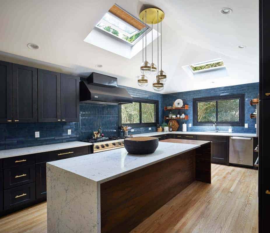 Dark blue modern kitchen with dark cabinets and dark appliances with a wood kitchen island with white counter tops, brightened with a skylight