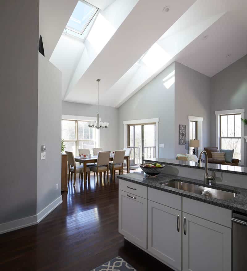 Modern looking kitchen and dining room with white cabinets and grey granite counter tops and stainless steel appliances and dark wood floors and skylight.