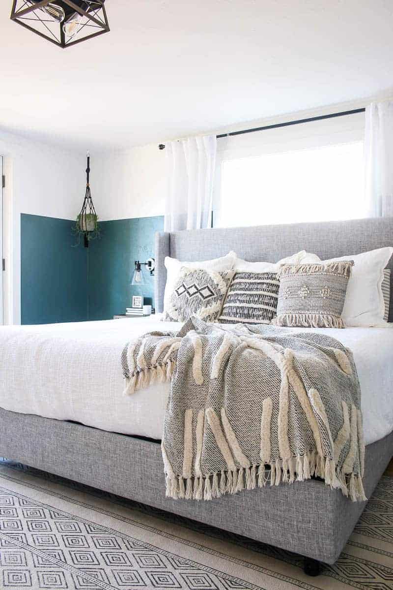 Our new king sized green boho bedroom is dressed with throw pillows and throw blankets, white linens, and an upholstered headboard.