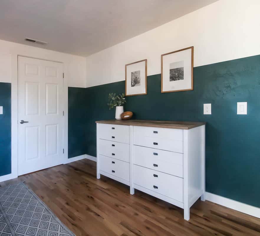 A corner of our master bedroom with a white dresser against a hunter green dresser. Two framed pictures hang over the dresser.