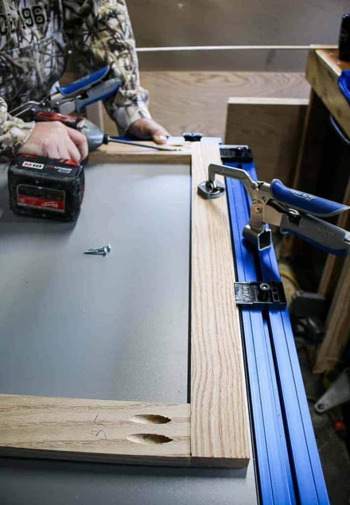 A clamp table is holding together a wooden face frame while a man is drilling in pocket hole screws