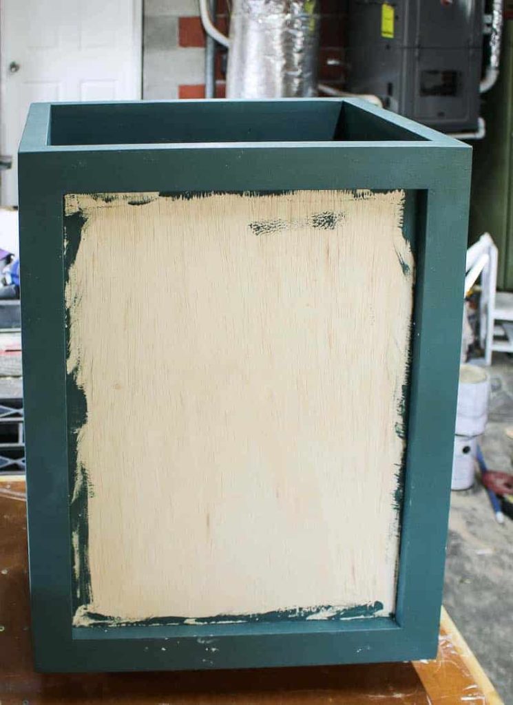 Painting the wooden laundry hamper with a dark teal paint