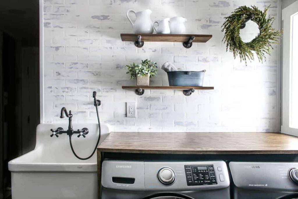 Farmhouse inspired laundry room with industrial-style shelving, a folding table over the washer and dry, and farmhouse sink