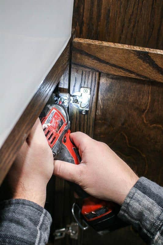 The man is skillfully installing the cabinet door by attaching the hinges.