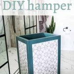 Laundry hamper with teal trim and gray and white tile sitting in a white bathroom with tile flooring and white walls. Text says how to build a diy hamper.