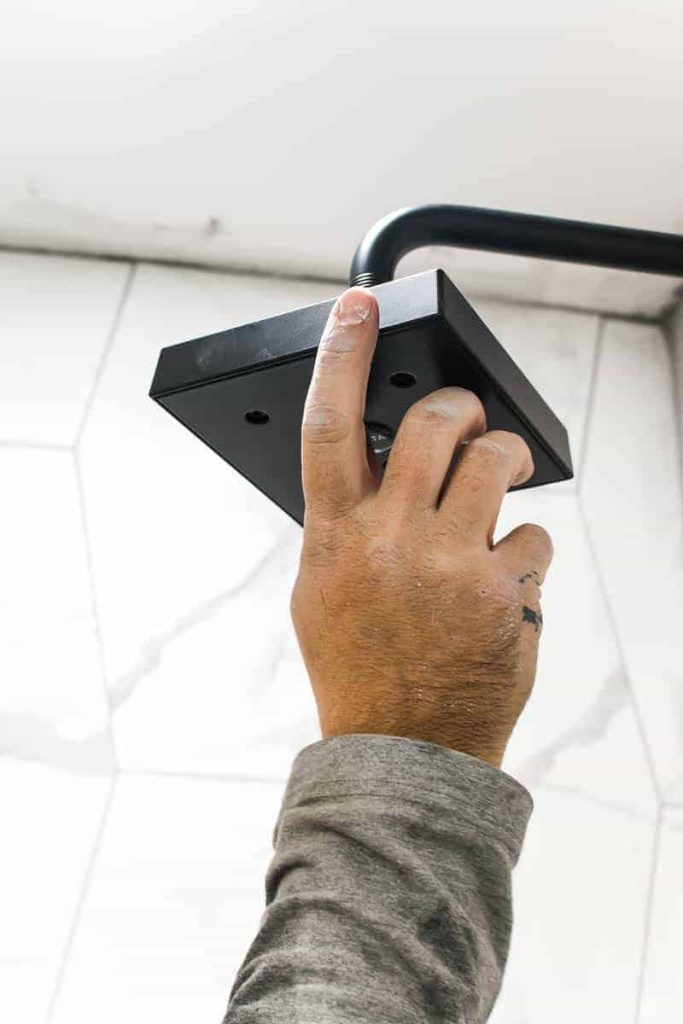 A hand in screwing in a black shower head with a backdrop of white marble tiles 