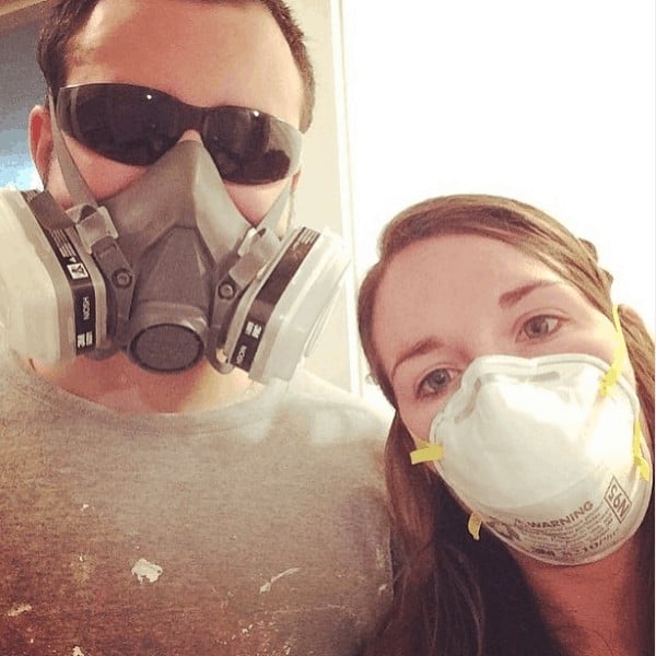 A selfie of a man and a woman, both wearing respirator masks, getting ready to start home renovations on an old house.