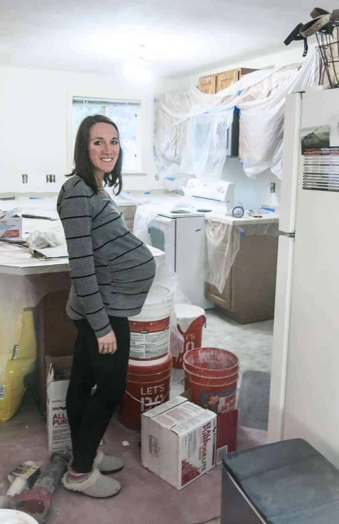 A very pregnant woman stands sideways, showing her pregnancy belly, in a kitchen that's undergoing home renovations.