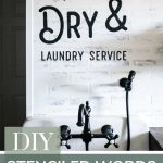 A face on view in a modern farmhouse laundry room with white walls and farmhouse sink with writing above on the walls that says wash and dry laundry service and says at the bottom with text overlay DIY Stenciled Words On Wall