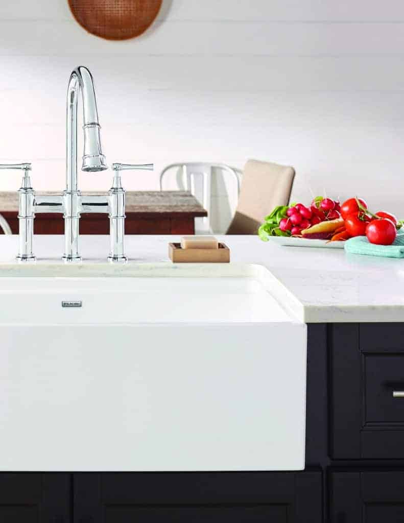 Shows a white fireclay farmhouse sink with stainless steel faucet in modern kitchen with fresh veggies on countertop