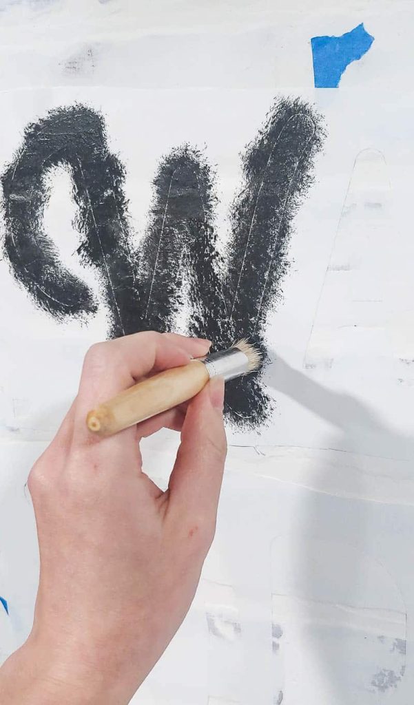 Using a stencil brush to carefully paint over the W of my DIY wall stencil, using a black paint.