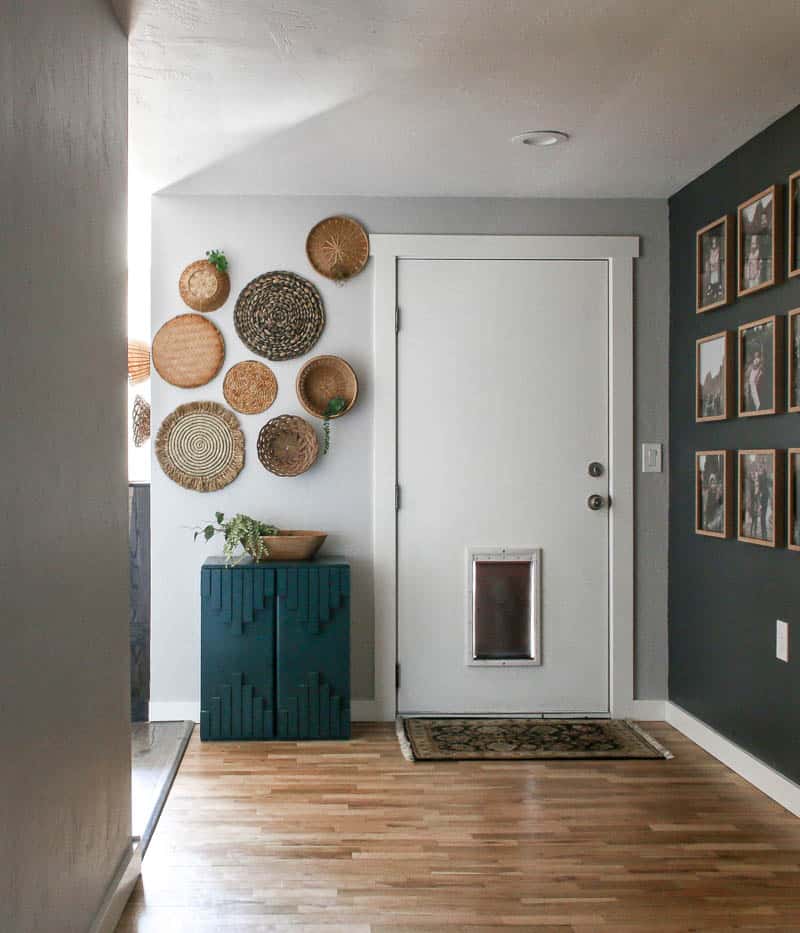 This boho-inspired entry way has an eclectic wicker basket wall created with thrifted wicker baskets, and a dark green boho cabinet