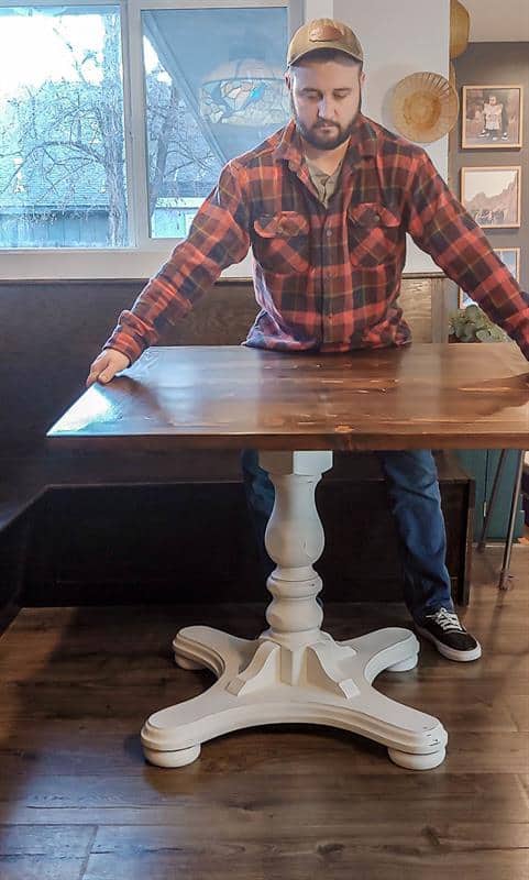 The table top is being securely attached to the base using screws, completing the assembly of the kitchen table.