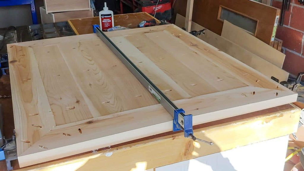 The miter-cut border slats are being attached around the table edge using wood glue and screws at pocket holes, forming the kitchen table top.