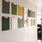 shows 12 gray, green, white, and yellow clipboards on a gray wall with a white live life simply frame in between the clipboards with overlay text that says clipboard wall