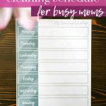 shows a weekly cleaning schedule on a wood table with pink flowers in the top corner with overlay text that says free printable cleaning schedule for busy moms, download here