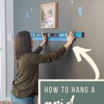 shows a woman using a level on a gray wall and marking where she is gonna hang photos in a wood frame with overlay texts that says how to hang a grid gallery wall