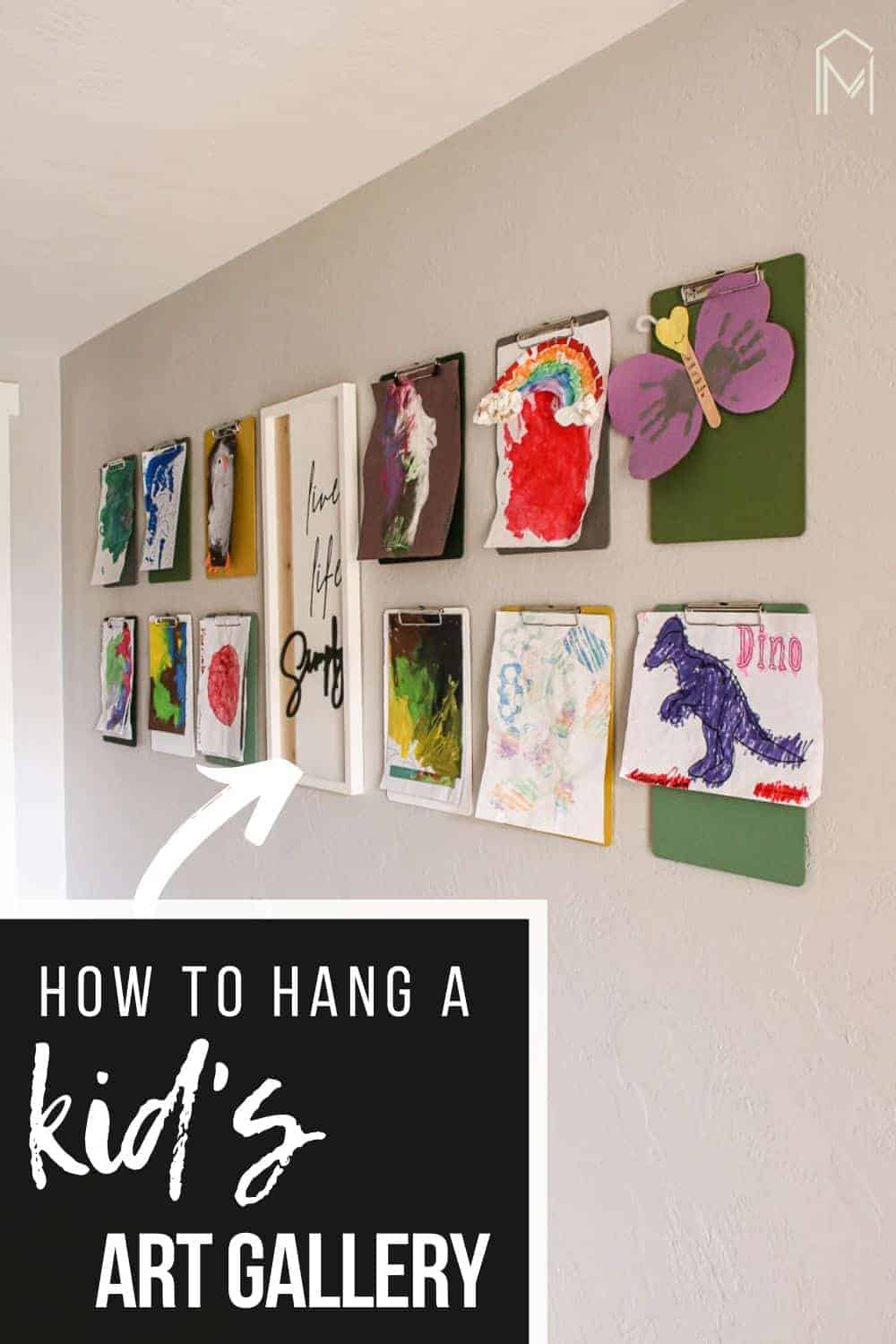 shows 12 clipboards with kid's paintings hanging from them on a gray wall with a live life simply frame hanging in between them with overlay text that says how to hang a kid's art gallery