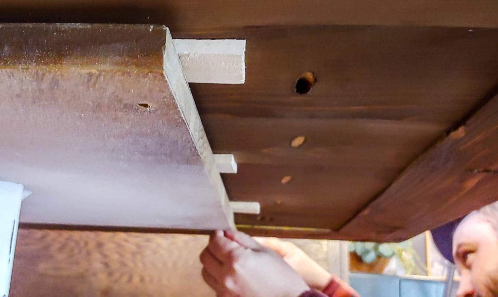 The man is checking to ensure that the table top is level, ensuring stability and proper alignment.