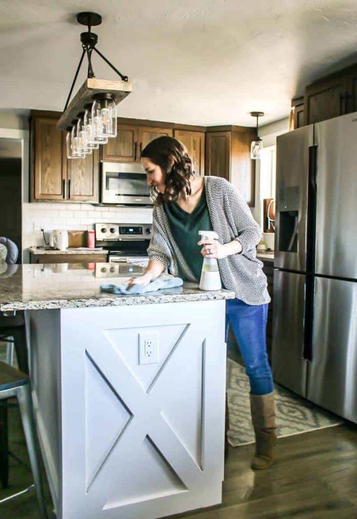 Cleaning a counter top with a spray bottle and towel in a kitchen with a white island and brown cabinets